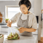음식물쓰레기 냄새 줄이는 법을 설명하는 여름철 주방에서 50대 한국인 여성이 음식물쓰레기의 물기를 빼고 밀폐해 정리하는 위생적인 장면